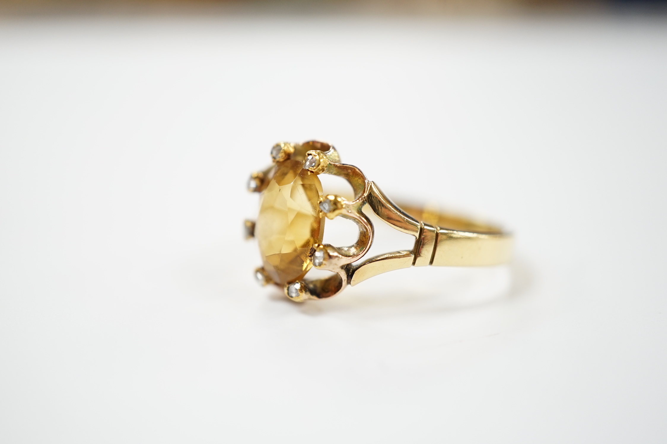 An 18ct and single stone oval cut citrine set dress ring, with eight stone diamond chip set border, size V